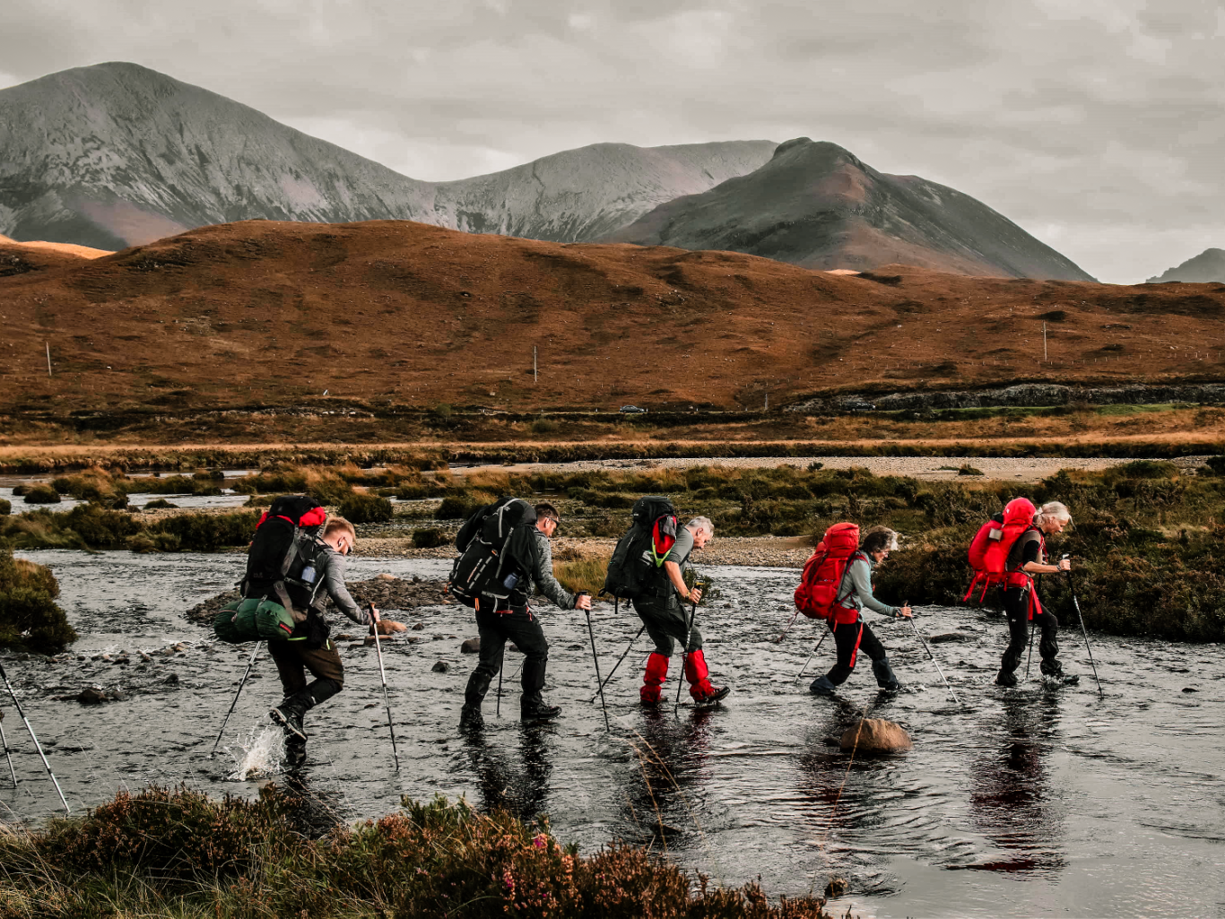 Hikers crossing a river below the Cuillin Mountains on the Isle of Skye, Scotland.