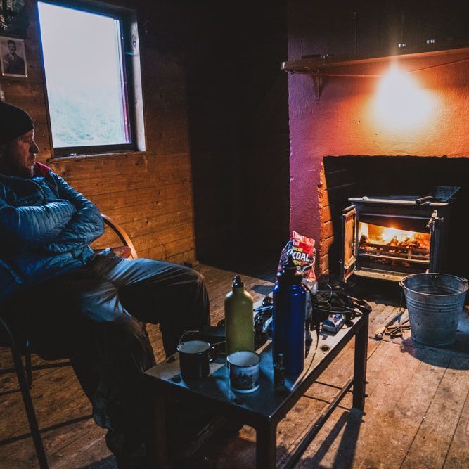 Hiker relaxing Hiker relaxing beside a wood-burning stove inside a traditional Scottish bothy.
